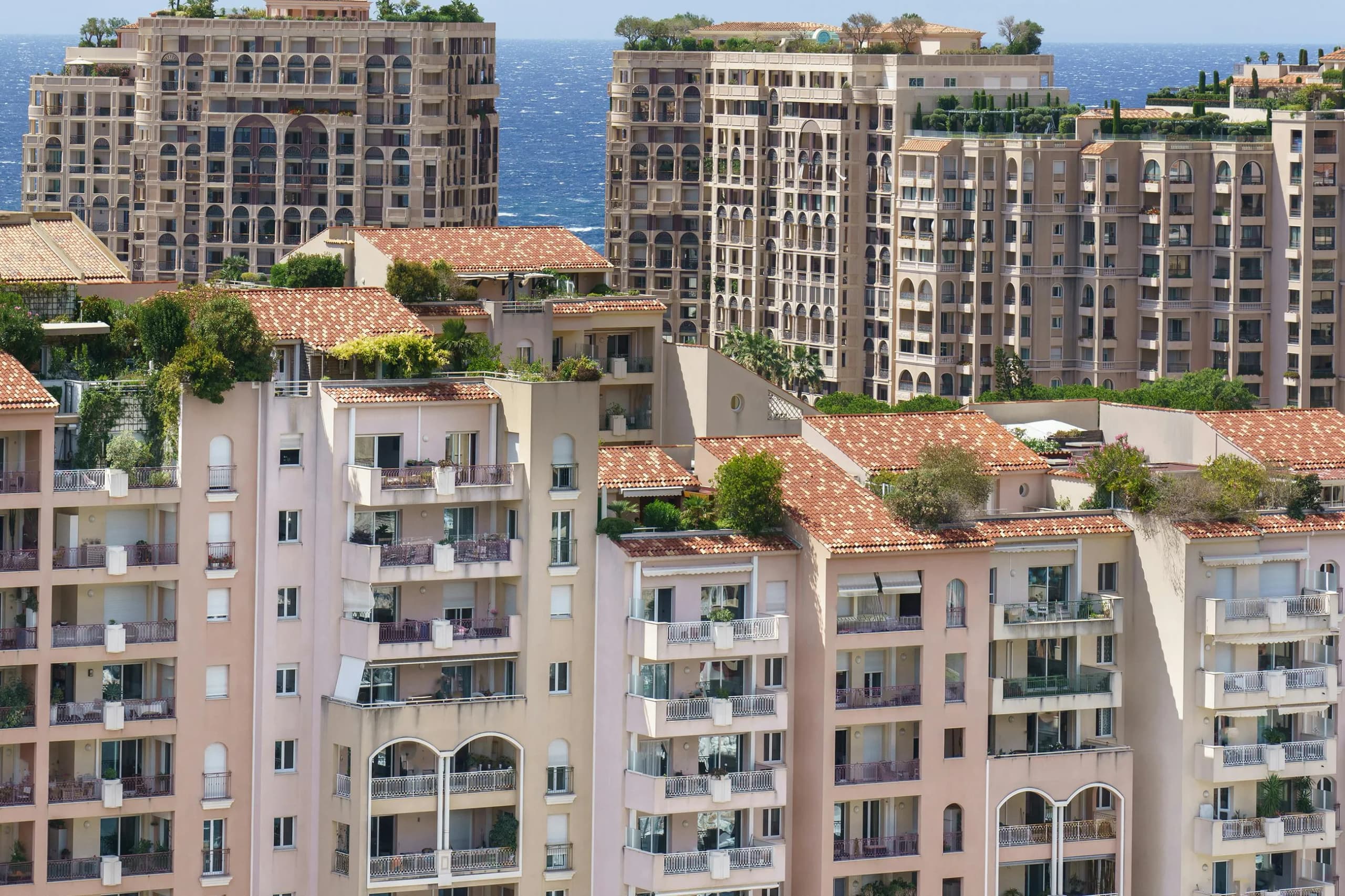 Monaco apartment buildings stacked up the hillside, balconies and roof terraces above the sea.