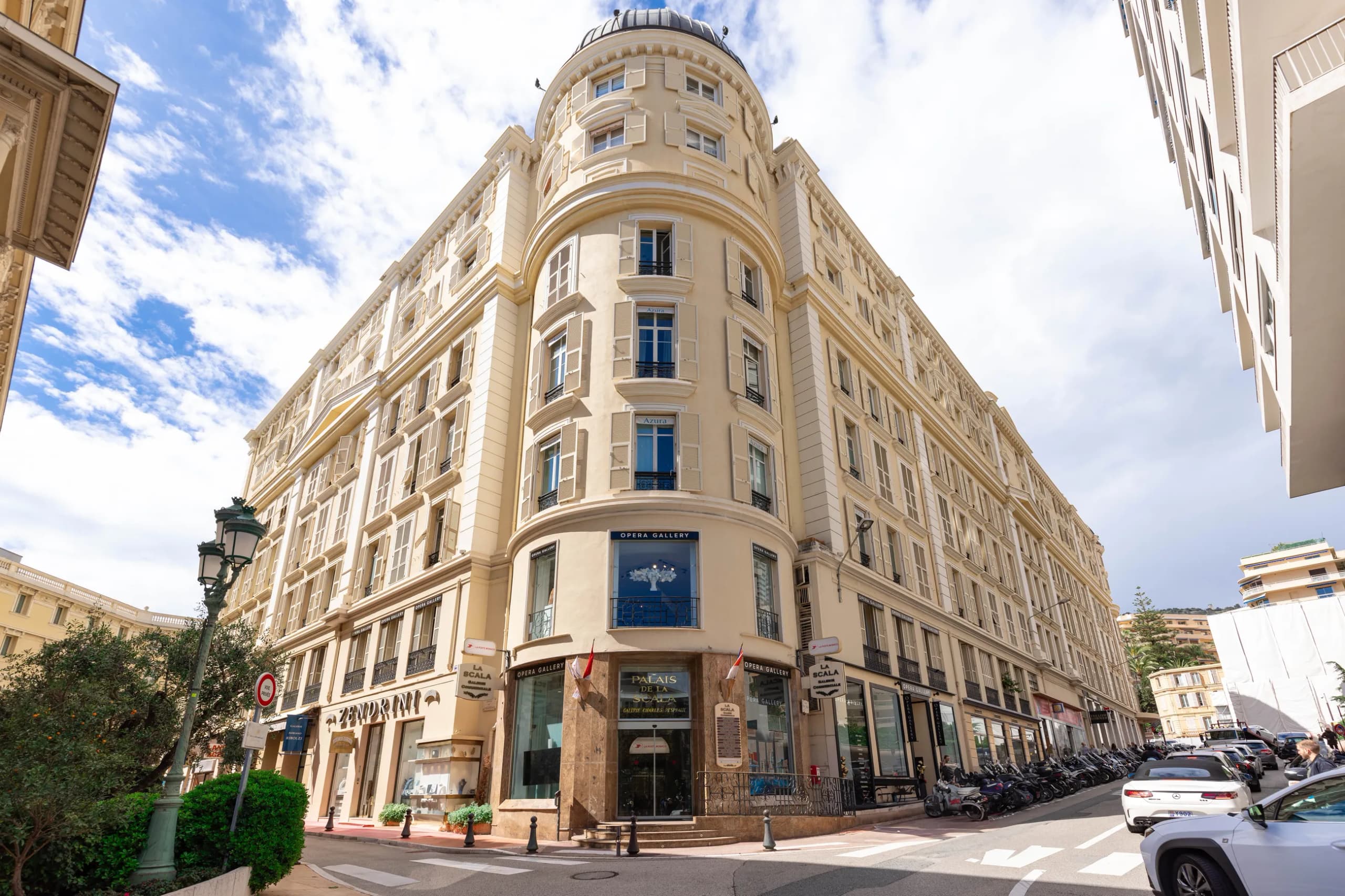 A belle-époque corner building in Monte-Carlo, shops at street level and a quiet road in front of it.